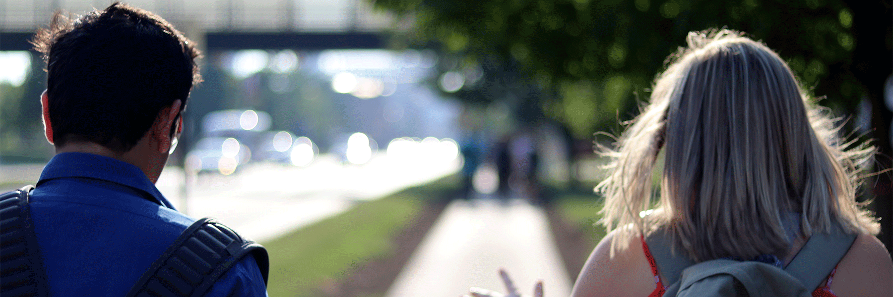 Close up picture of two students walking on a side walk on campus with their backs facing the camera. 